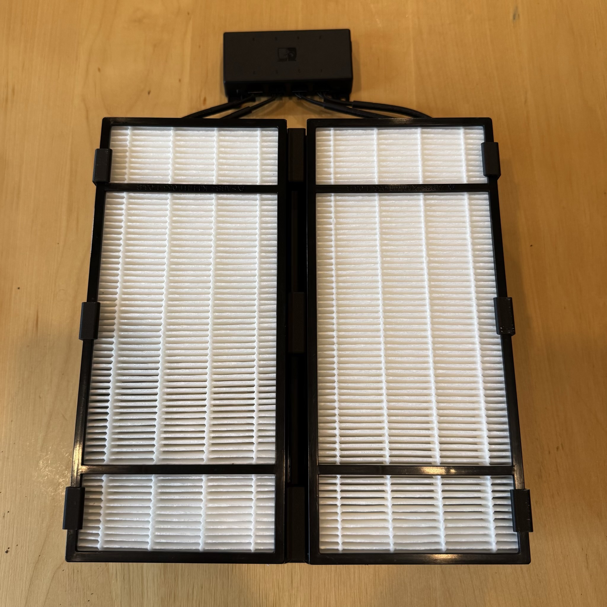 Two white HEPA filters are attached to a cowl below. Four wires snake up the sides and meeat at a black box at the top.