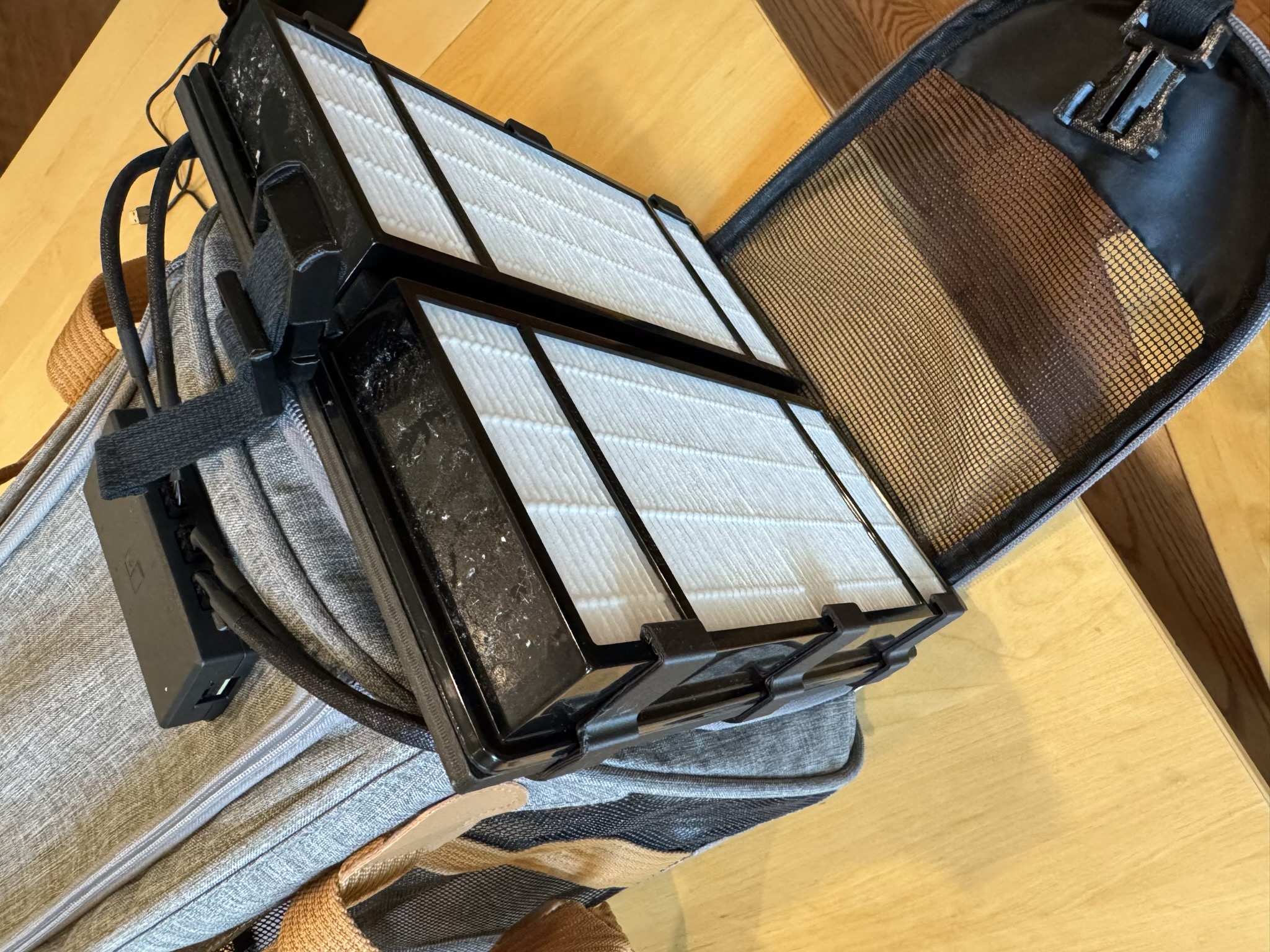 The full filter assembly is placed at one end of the cat carrier. The HEPA filters are facing outward, and the halves of a side-release buckle are visible.